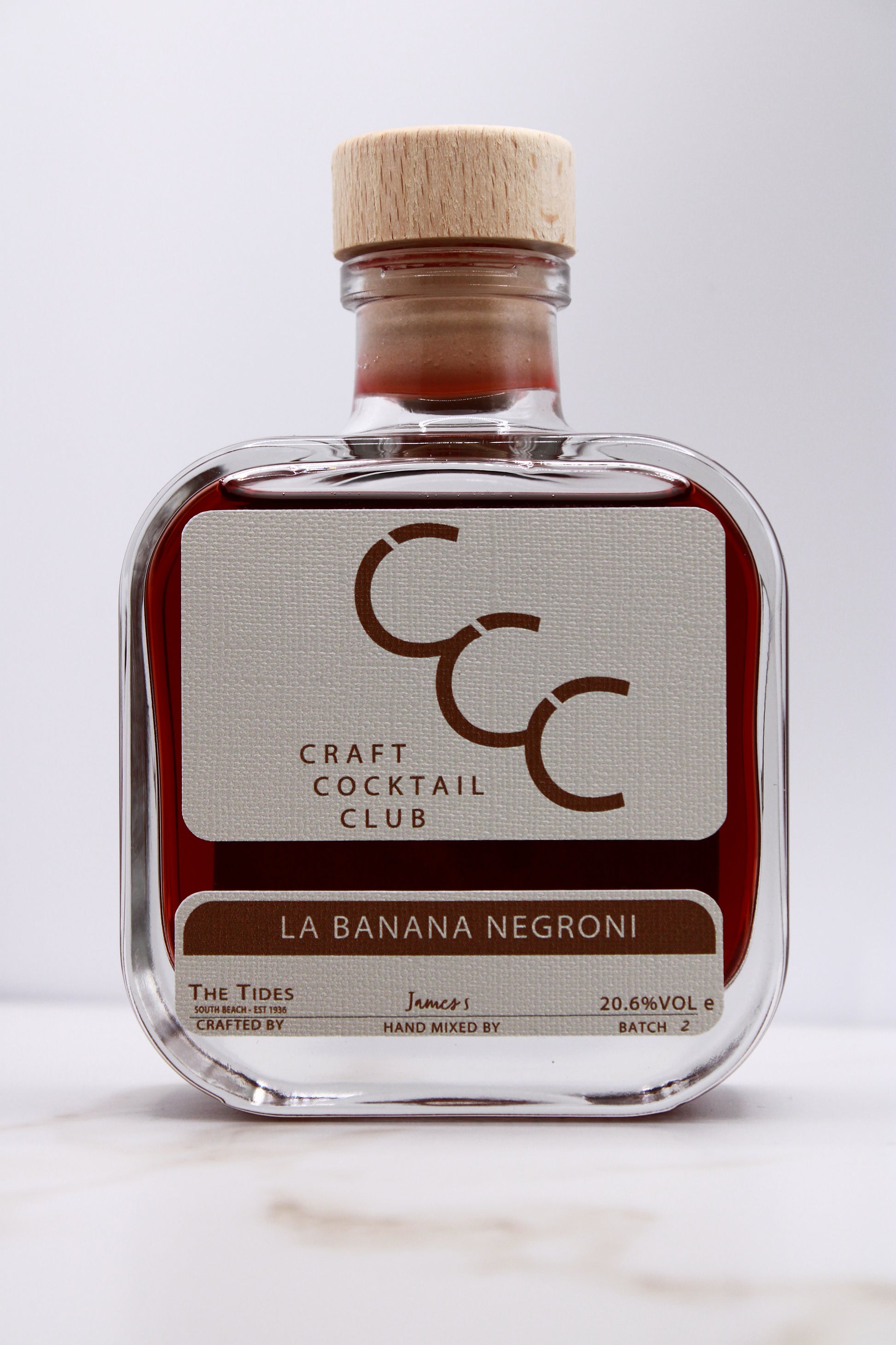 picture  of a craft cocktail club square glass bottle with a light brown label that reads Banana Negroni 