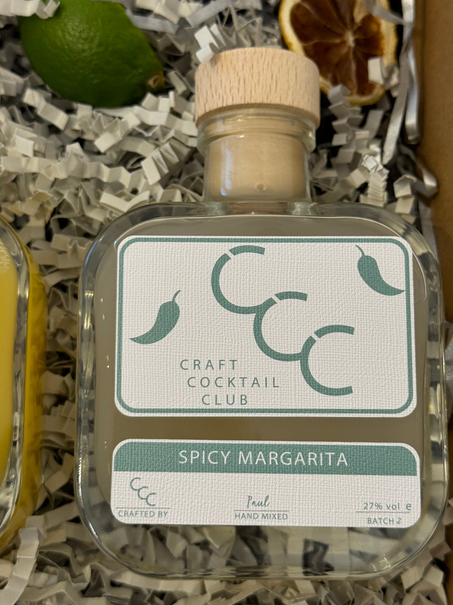 picture of a craft cocktail club square glass bottle, with green liquid in a gift box, label says spicy margarita 