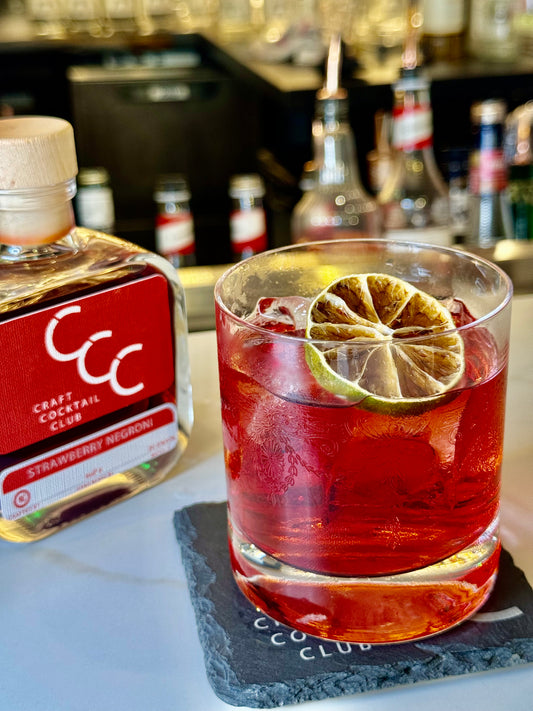 picture of a  bright red negroni on ice next to a bottle on a bar 