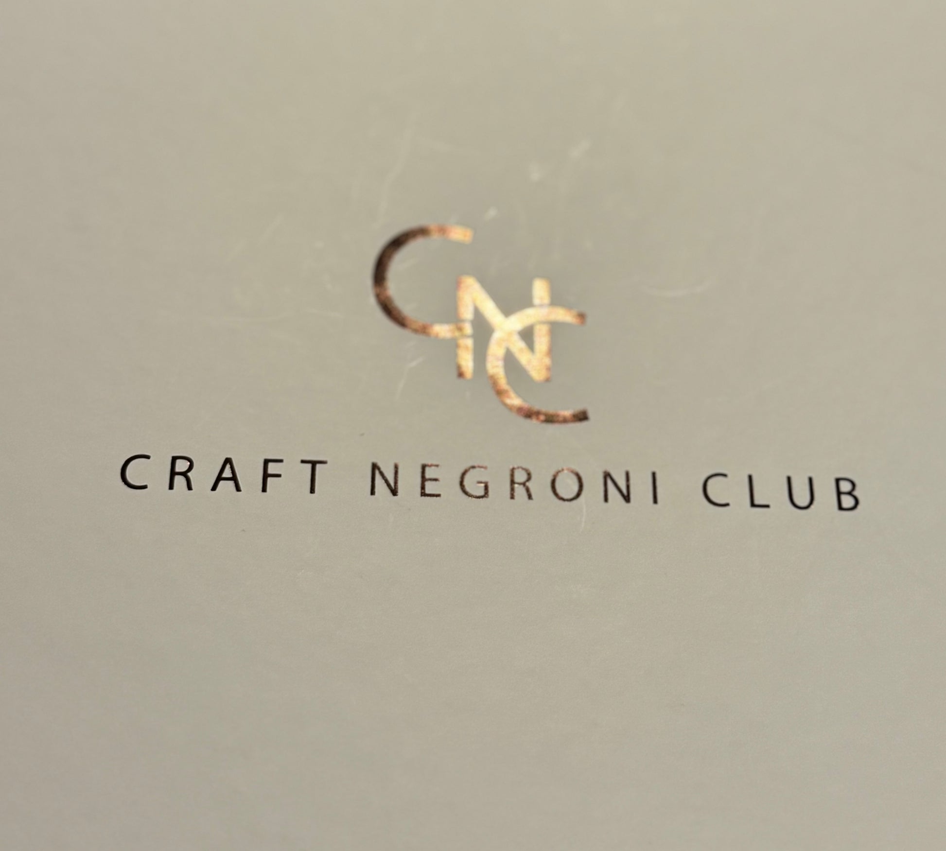 Picture of a close up of a gift box label, logo is metallic shiny bronze and reads Craft Negroni Club 