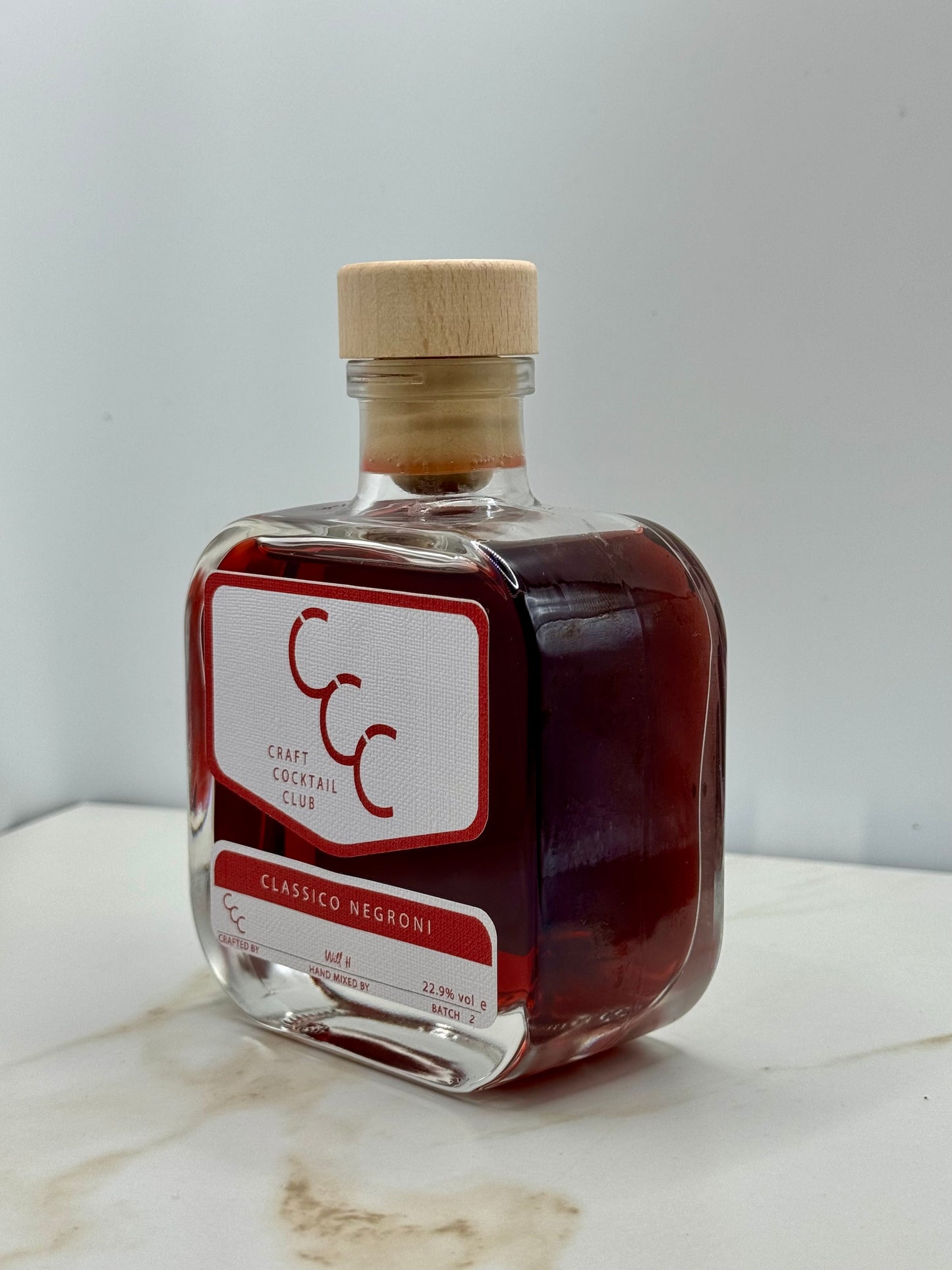 Picture of a bottle of pre mixed negroni, the bottle is square and had a deep red liquid inside. Label reads Craft Cocktail Club. Classico Negroni 