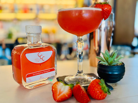 Picture of a bottle of ready to drink cocktail next to a margarita glass with red liquid and strawberry garnish 