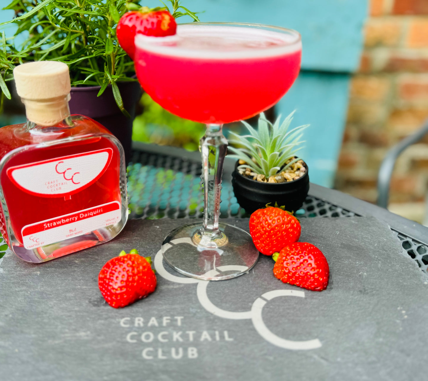 Picture  of a strawberry daiquiri on a slate outside with a strawberry on the rim 