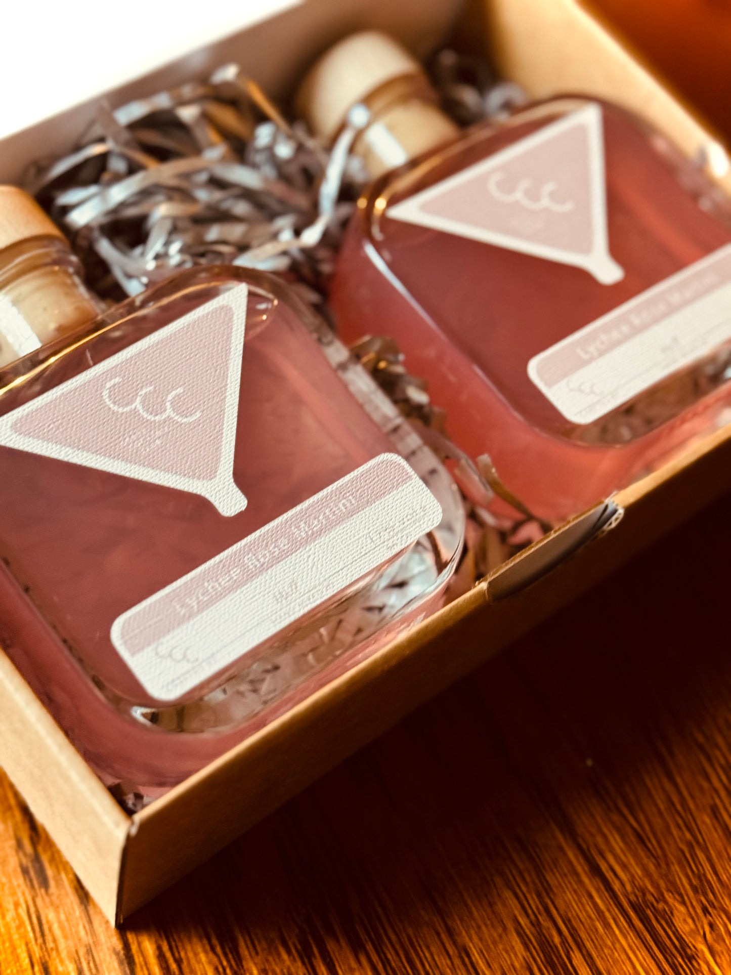 Picture of two pink bottles of Cocktails in a  gift box with Dark wood table as the background 