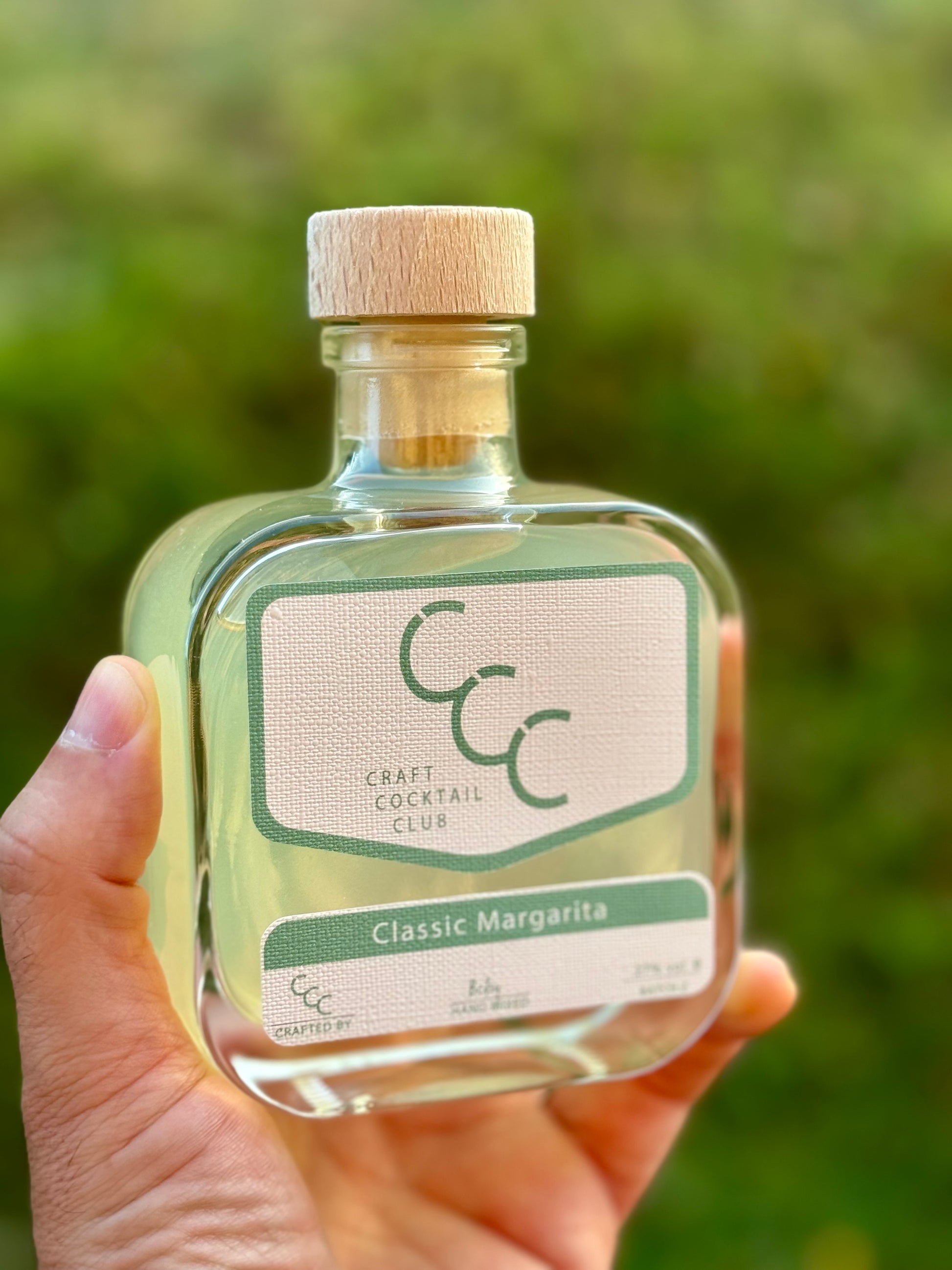 Picture of a craft cocktail bottle in mans hand with green grass background 