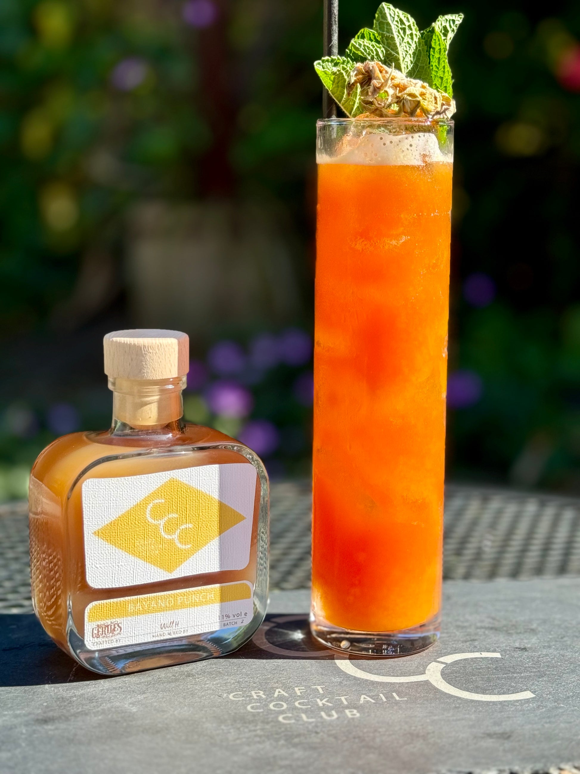 picture of a Rum Punch outside on a sunny day next to a pre made cocktail bottle 