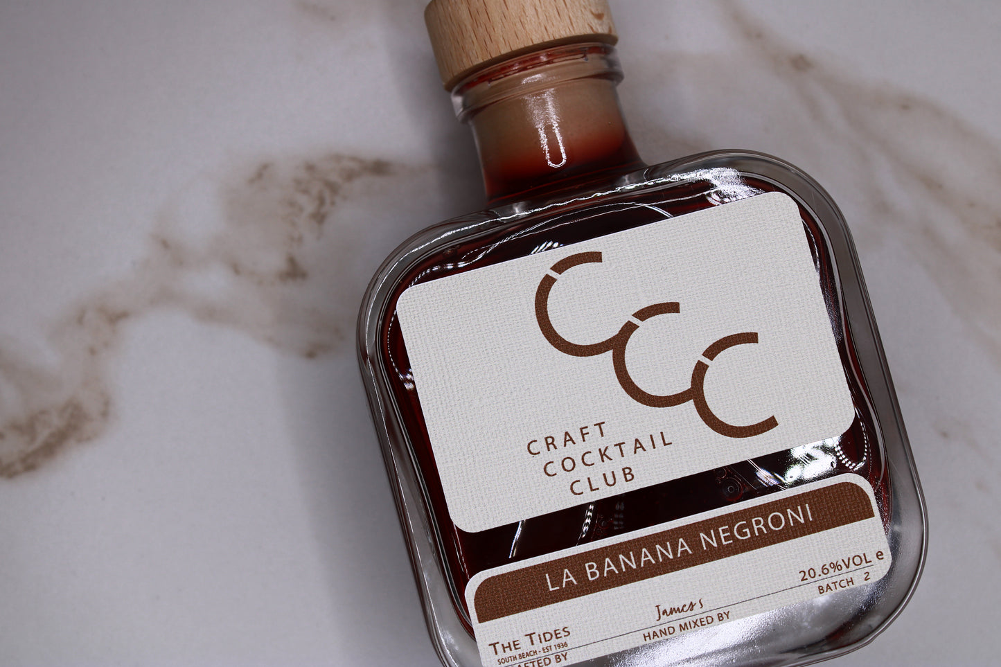 Picture of a craft cocktail club bottle flat against a cream tiles, table reads Banana Negroni 