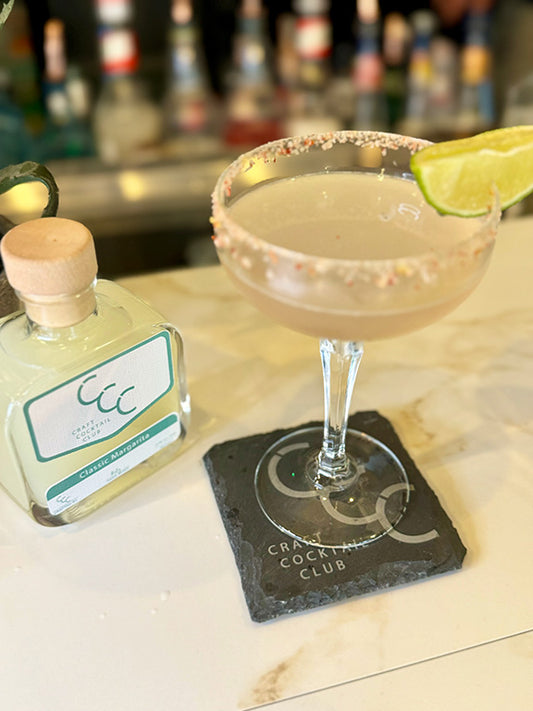 picture of a margarita glass with a lime on the edge on a coaster next to a pre made margarita bottle 