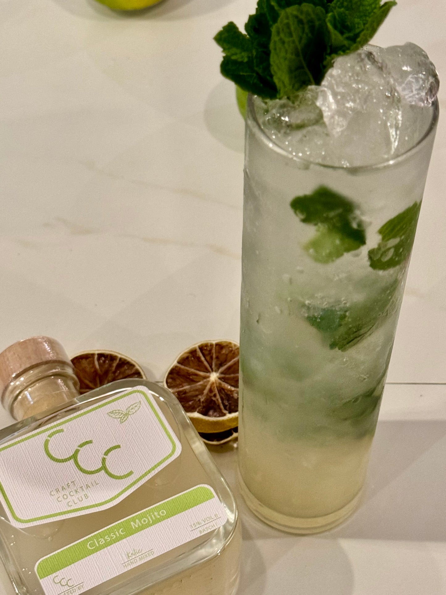 Picture of  bottle of ready to drink cocktail in a square glass bottle, sat on a marble bar. 