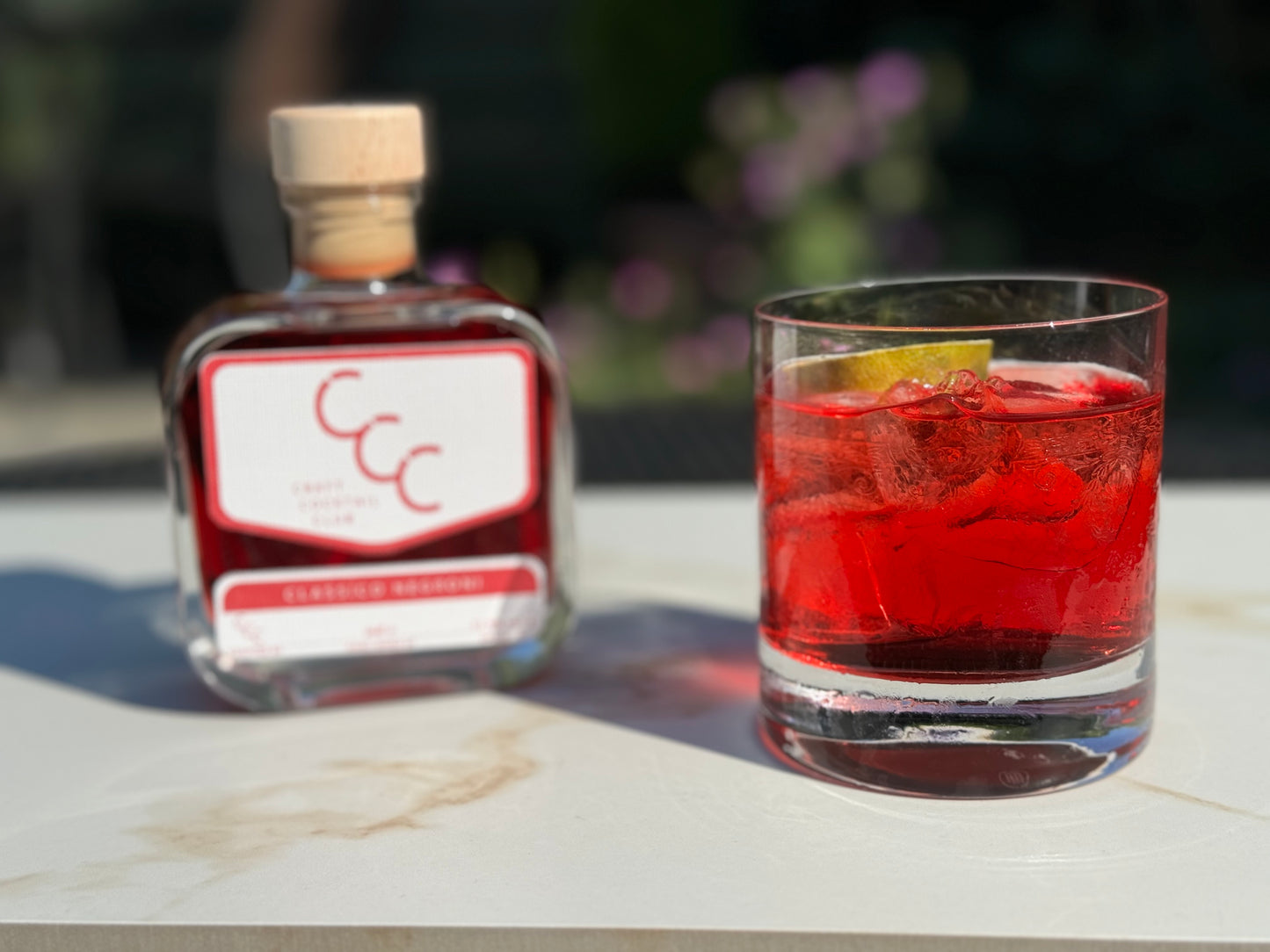 picture of a negroni next to a craft cocktail club bottle outside on a sunny day 