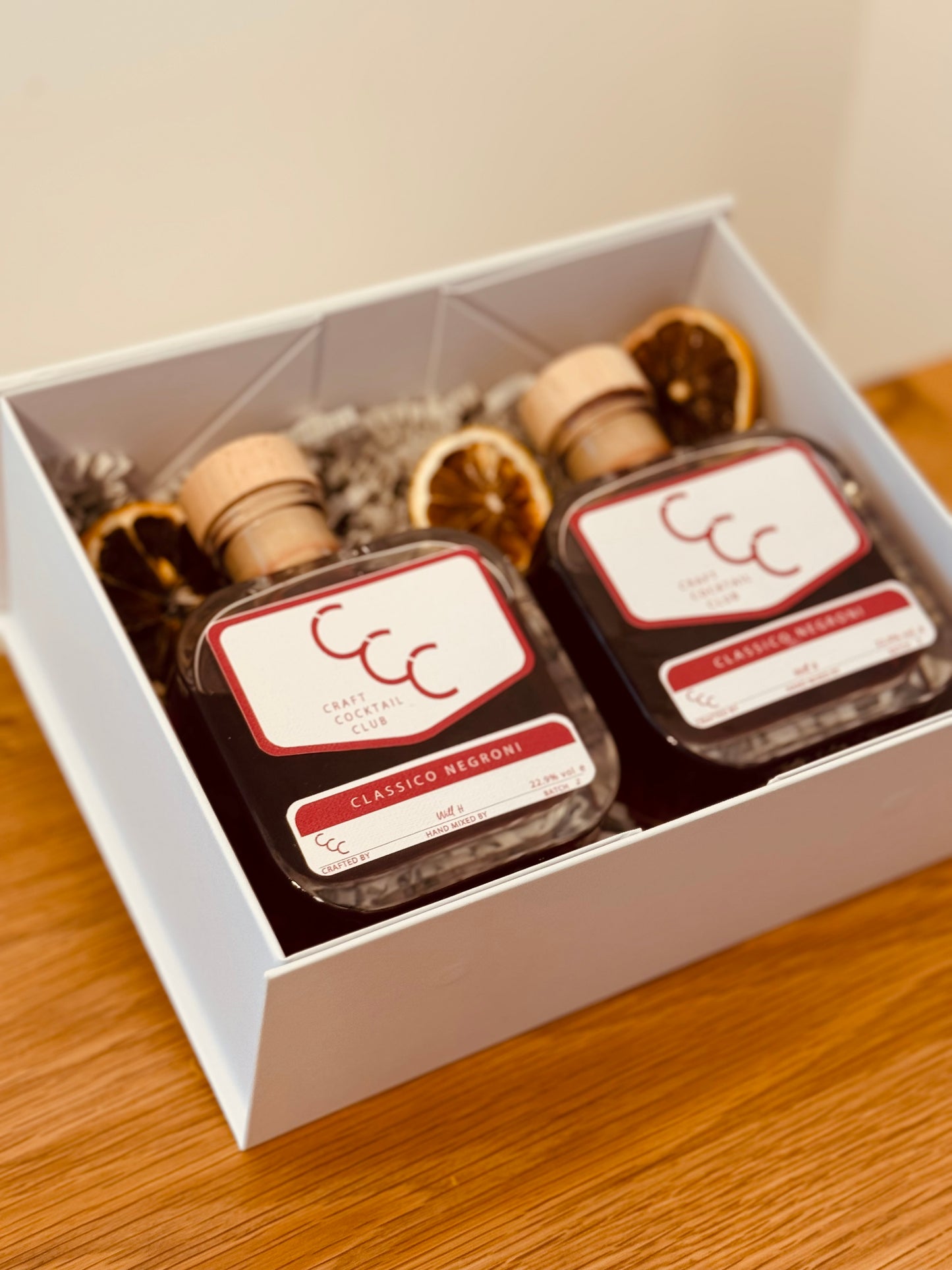 Picture of a gift box of two ready to drink negroni sat together in a gift box on and oak table with dried oranges next to the bottles 