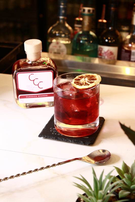 Picture of a classic negroni on a marble bar with a square glass bottle of red liquid label reads Craft Cocktail Club, Classic negroni 