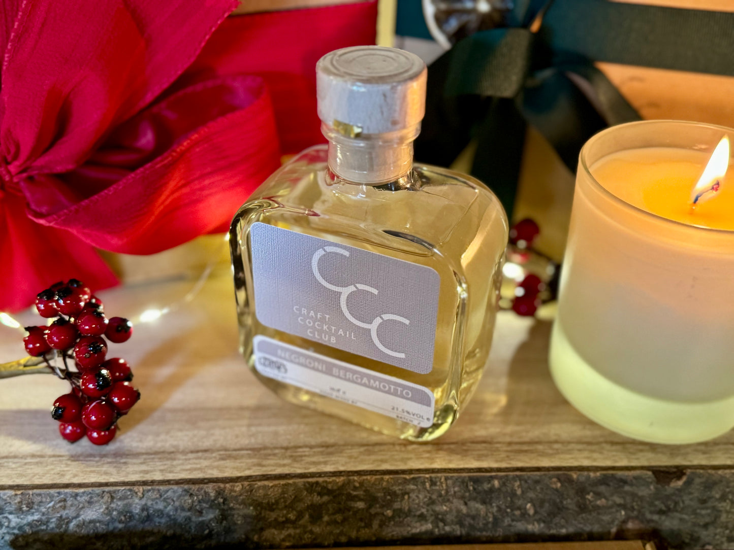 A picture of a negroni Bianco next to a candle surrounded by christmas gifts with red and green ribbons 