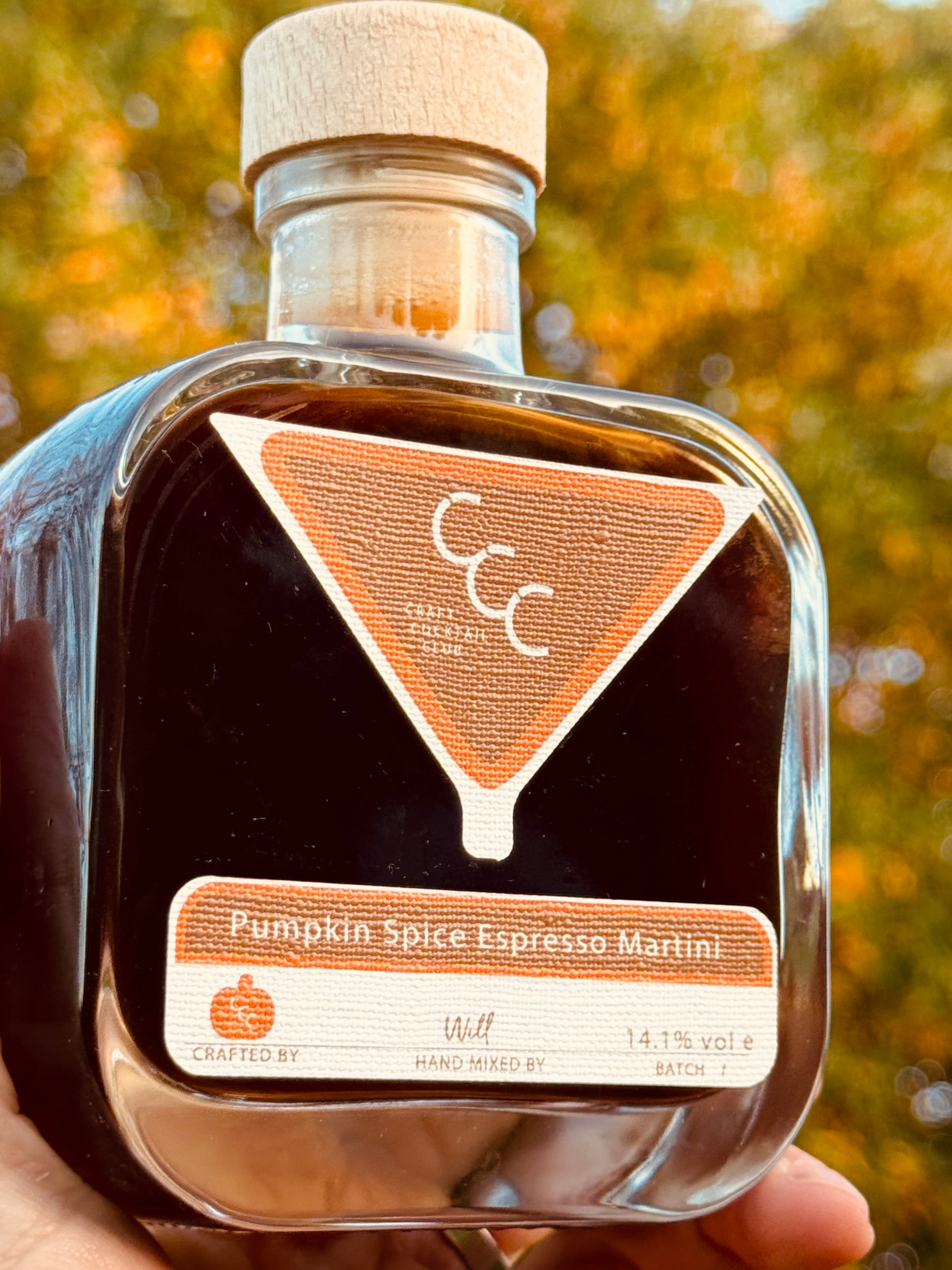 picture of a hand holding up and bottle of espresso. martini against autumn leaves in the background, label reads Craft Cocktail Club Pumpkin spice espresso martini 