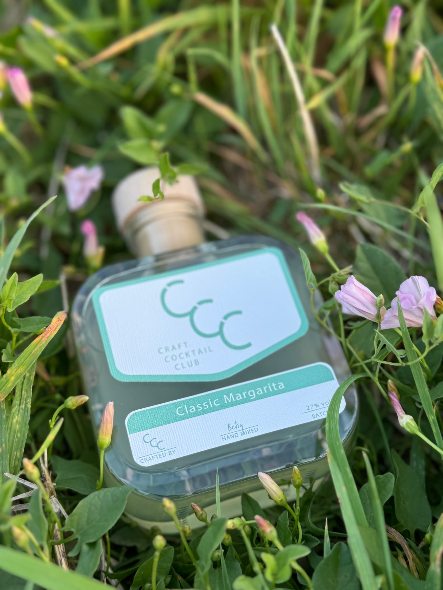 picture of a bottle of margarita from craft cocktail club in some grass on a sunny evening 