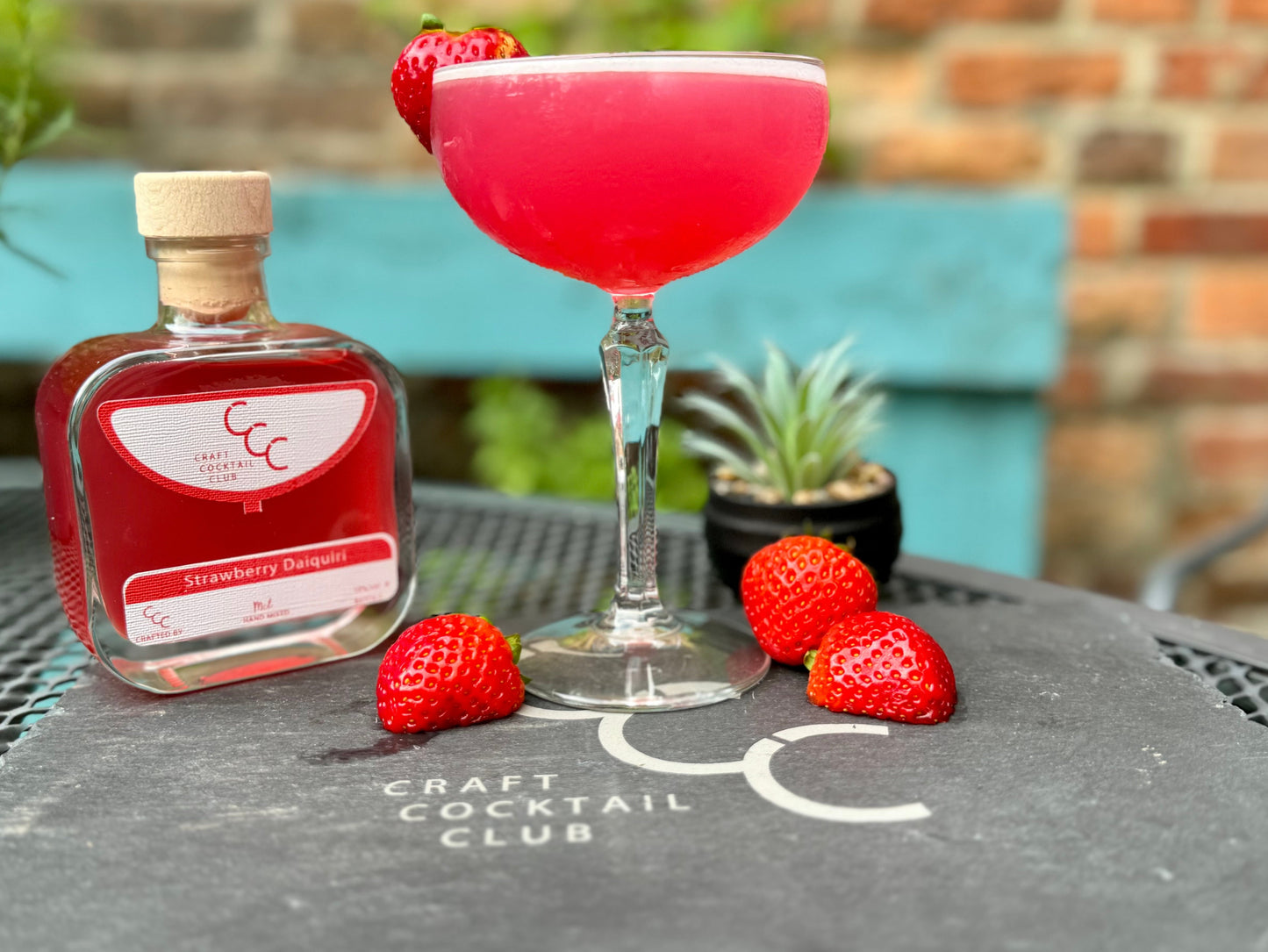 picture of a strawberry daiquiri outside with strawberries around the base of the glass